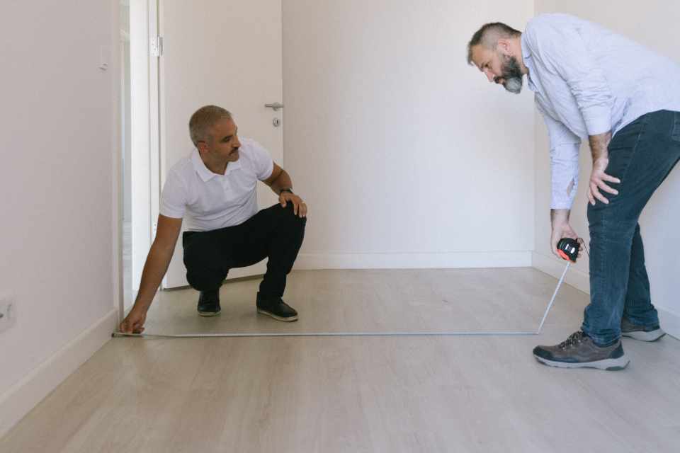 two men using measuring tape to measure square footage of room